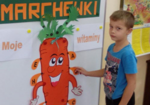 Chłopiec przy tablicy wskazuje witaminy, które zawiera marchew.